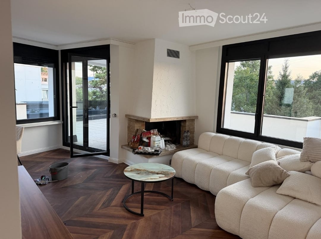 Modern living room with large windows offering a scenic view, a fireplace, a white sectional sofa, and a round coffee table.
