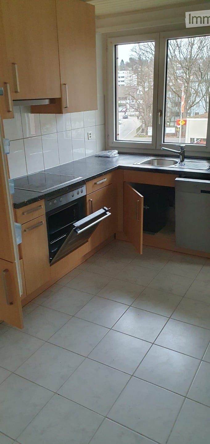 Modern kitchen with light wooden cabinets, tiled floor, stainless steel oven, and sink.