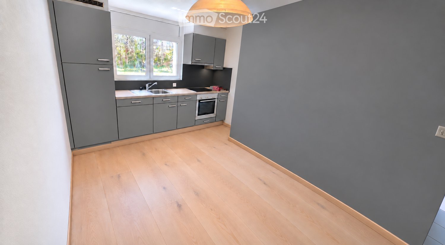 Modern kitchen with grey cabinets, light wooden flooring, and a window overlooking greenery.