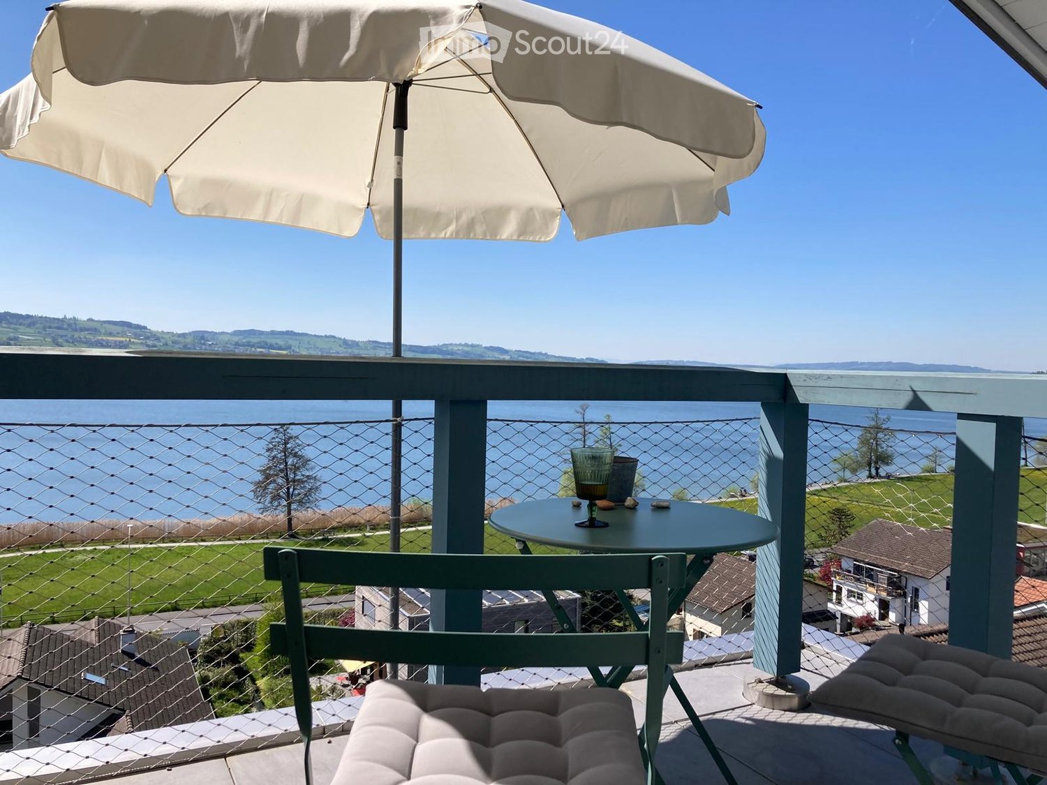 Balcony with a view of a lake and surrounding landscape, featuring a round table, chairs, and an umbrella.