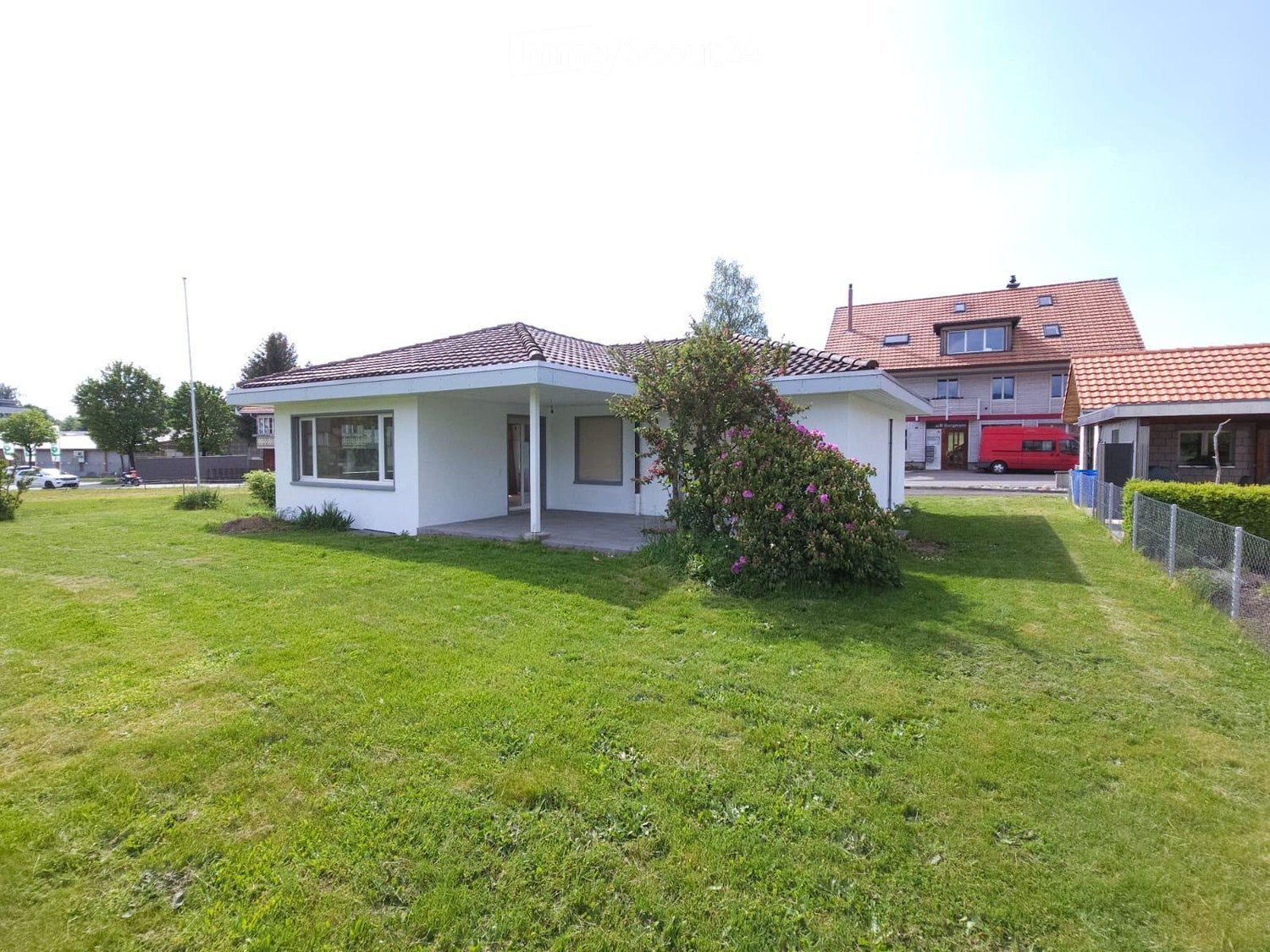 Single-story house with a red-tiled roof, white exterior, and a well-maintained lawn in front.