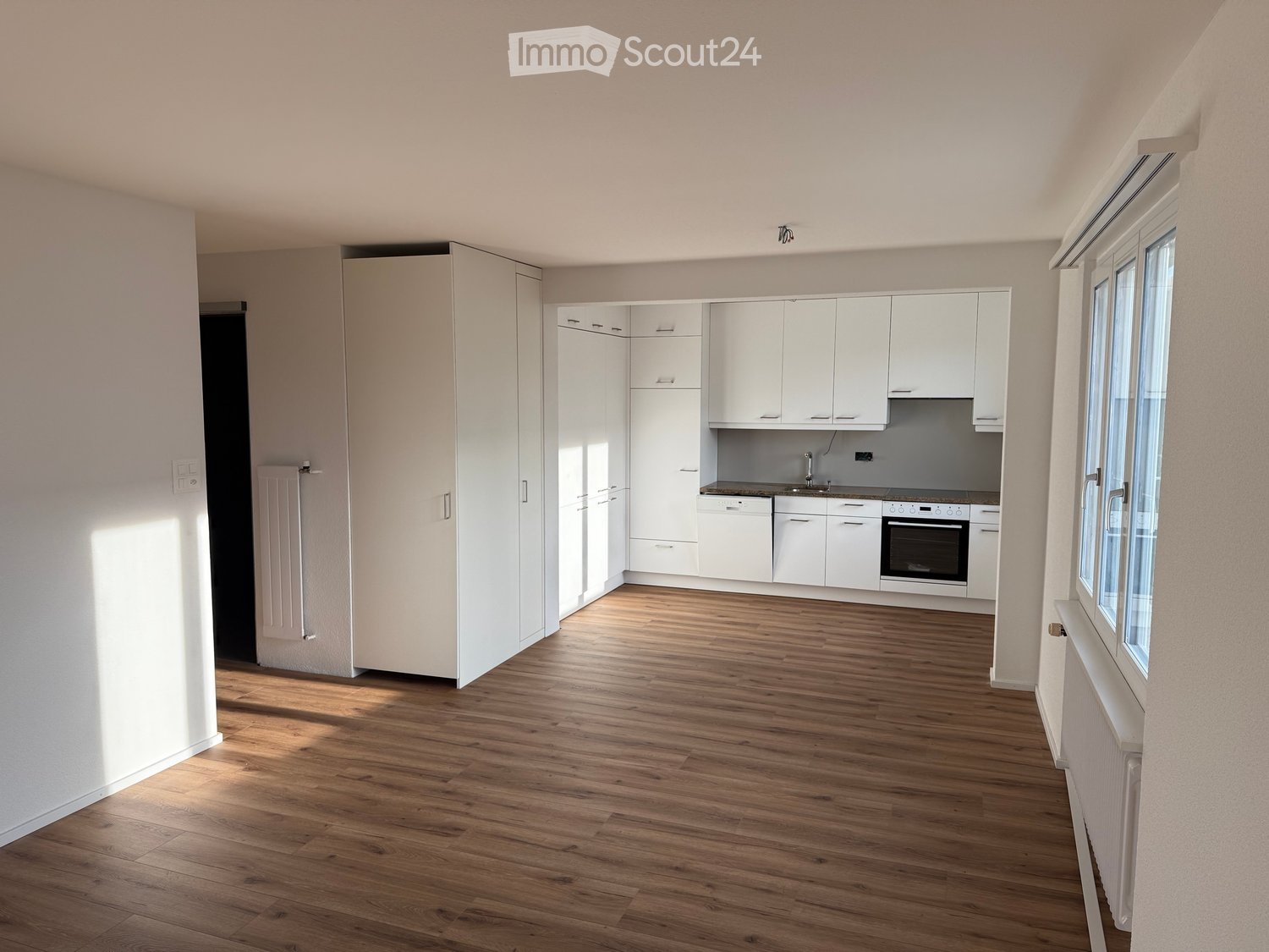 Bright, modern kitchen with white cabinets, wooden flooring, and built-in appliances including a sink, oven, and dishwasher.