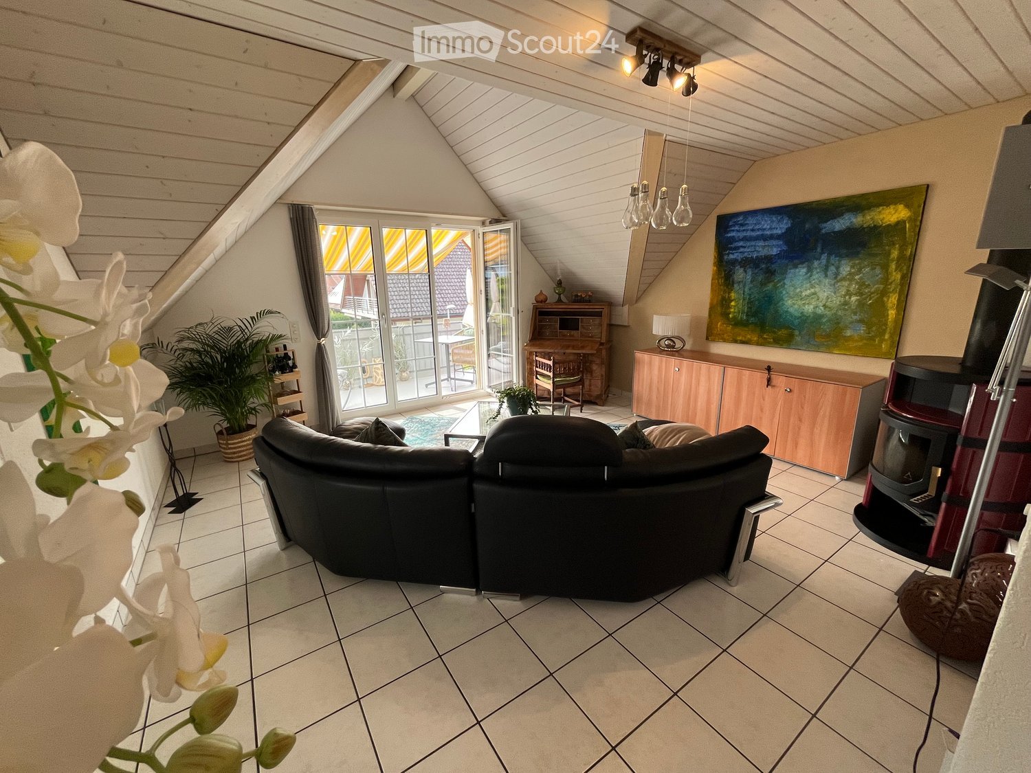 Bright living room with a black sectional sofa, coffee table, wooden cabinet, and a fireplace. Large windows offer a view of the garden and pool.