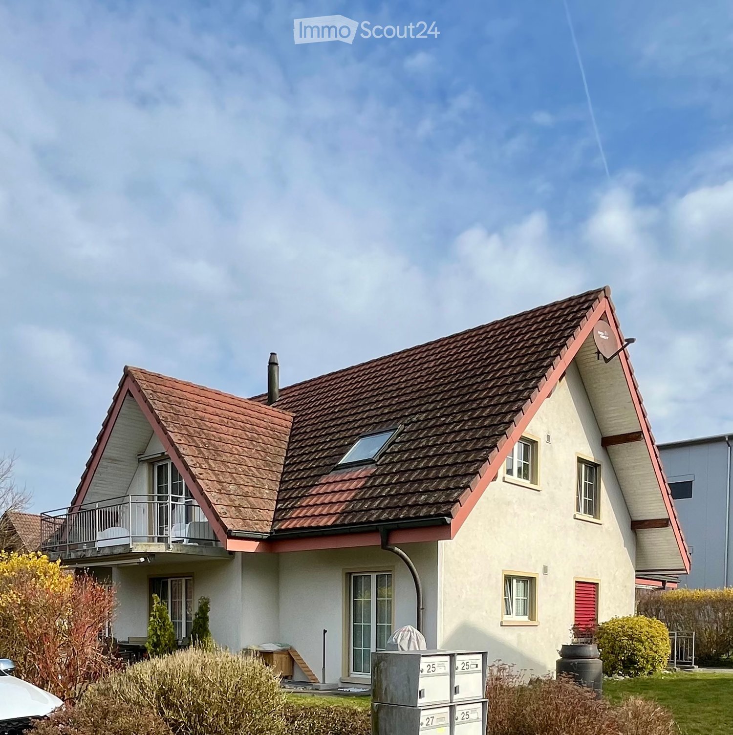 Two-story house with a red-tiled roof, white walls, and a balcony on the upper level. The house features multiple windows and a satellite dish on the roof.
