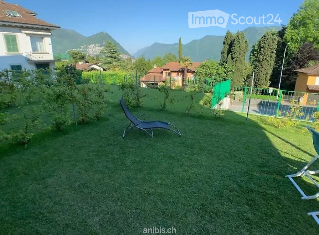 Well-maintained garden with green grass, lounge chairs, and a scenic mountain view in the background.