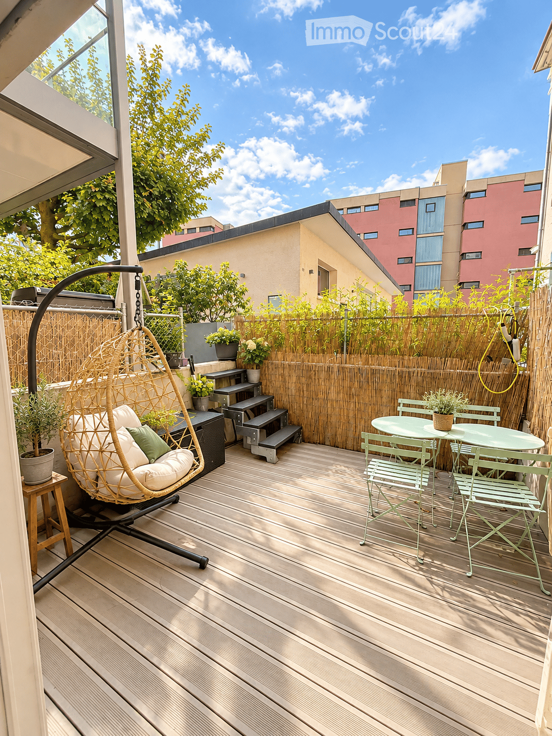Wooden deck with a hanging egg chair, small table with chairs, potted plants, and a bamboo privacy screen.