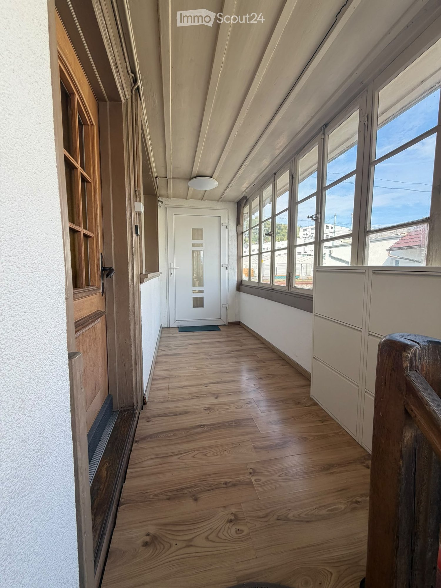 Empty hallway with wooden flooring, white walls, large windows, and a central door leading to another room.