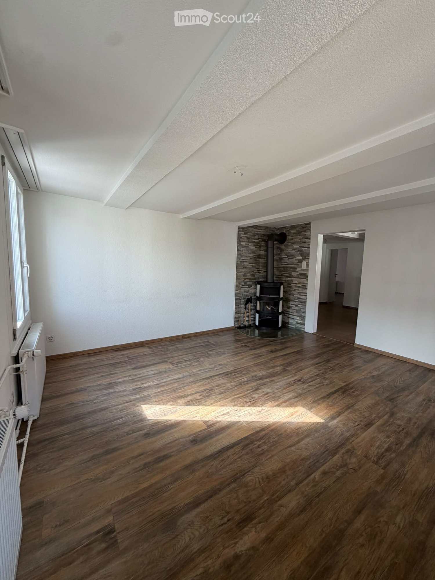 Empty room with wooden flooring, white walls, and a fireplace in the corner.