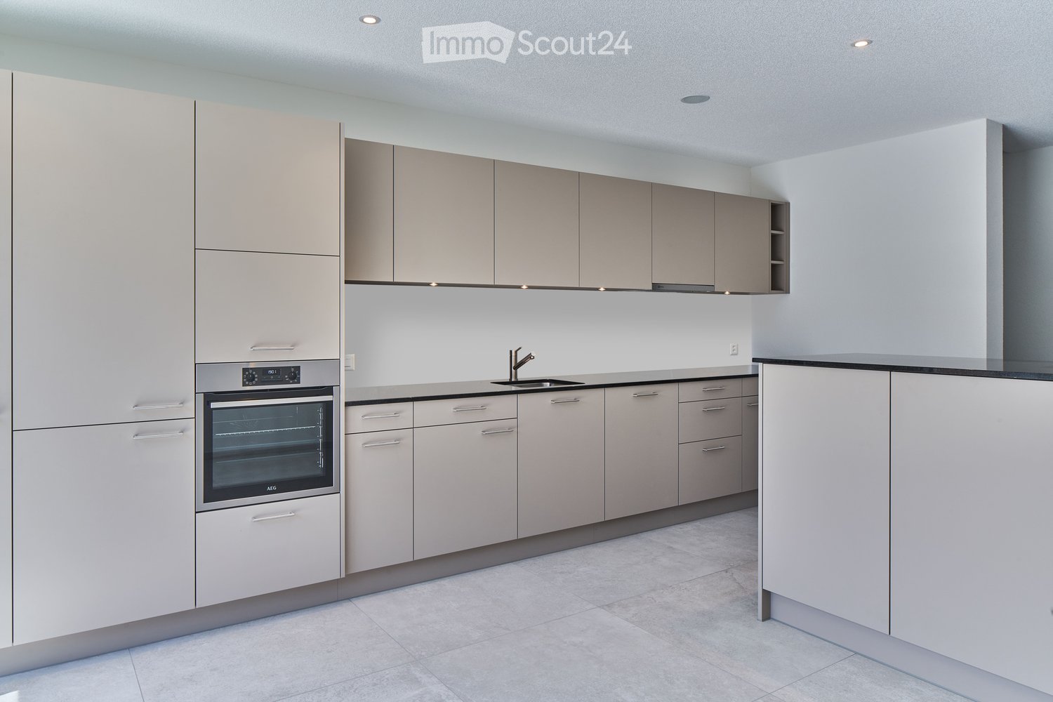 Modern kitchen with light grey cabinets, stainless steel oven, and a black countertop.