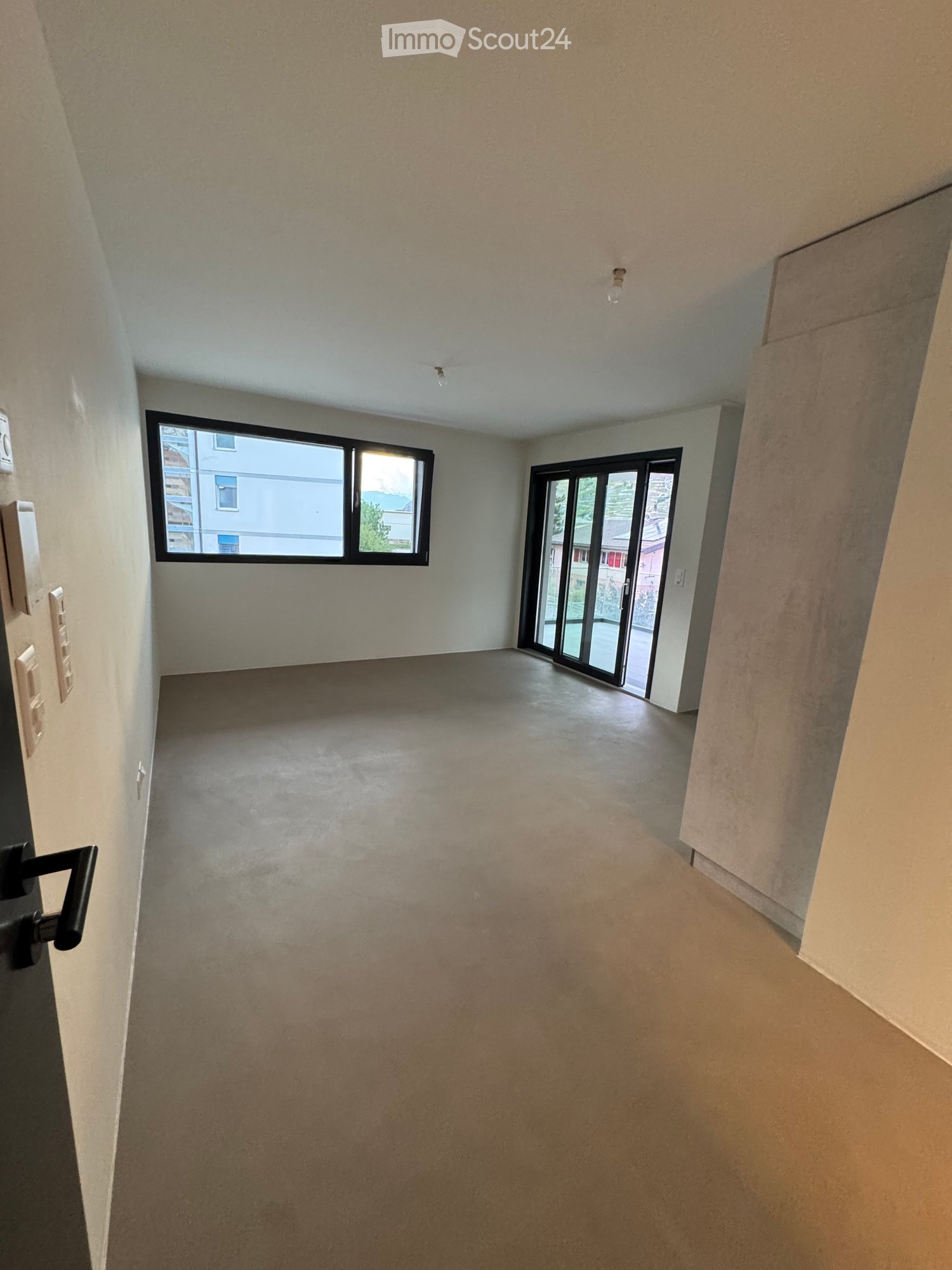 Empty room with concrete floor, white walls, large window, and sliding glass door leading outside.