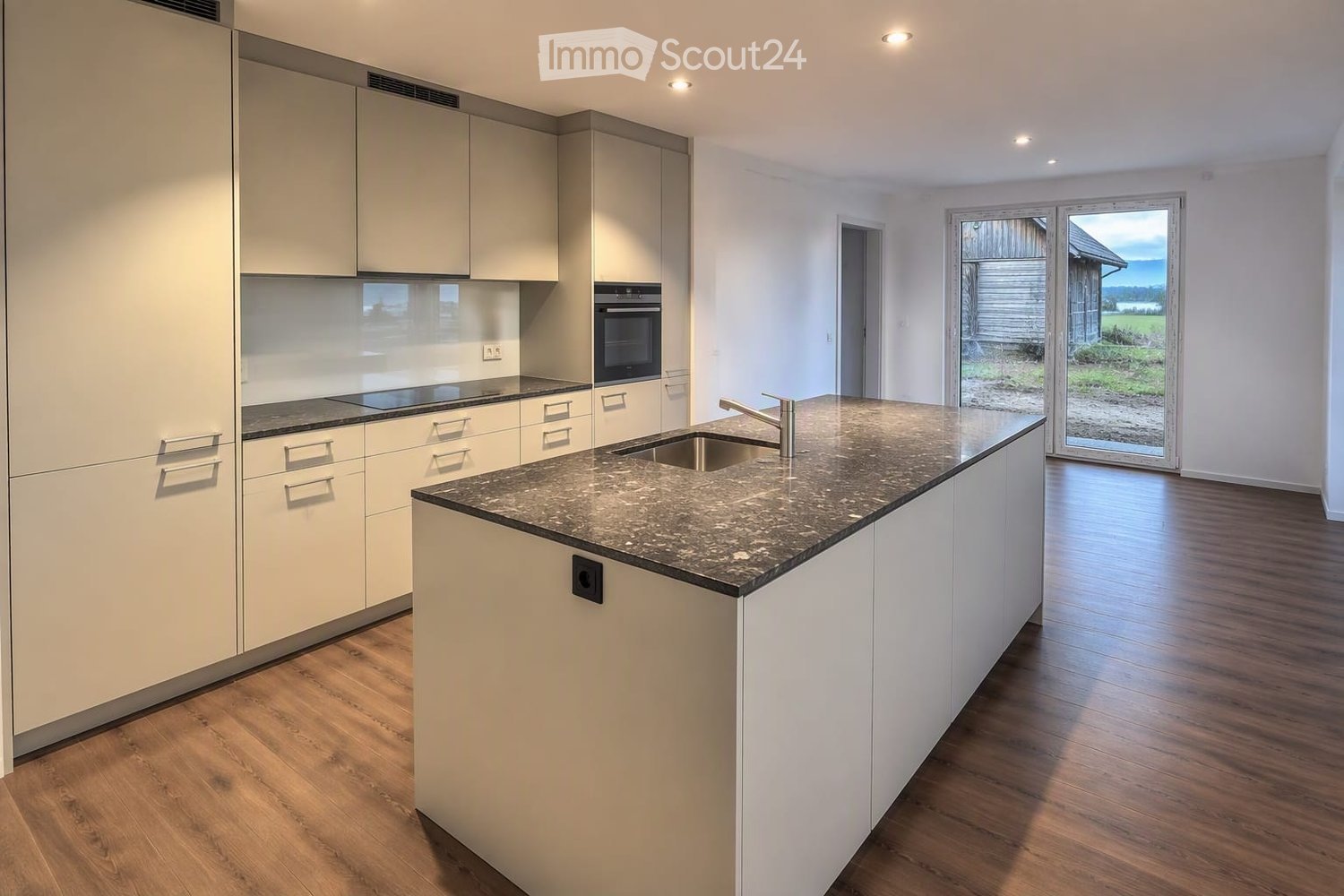 Modern kitchen with white cabinets, granite countertop, sink, and oven. Large sliding glass door leads to outdoor area.