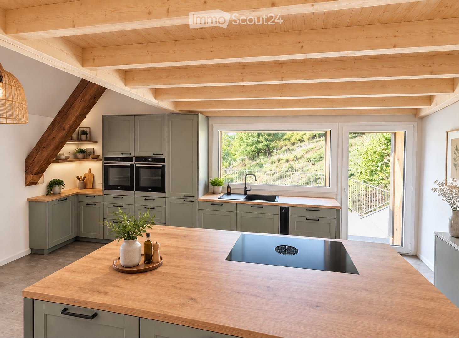 Modern kitchen with grey cabinets, wooden island, induction cooktop, double oven, and large windows overlooking a garden.