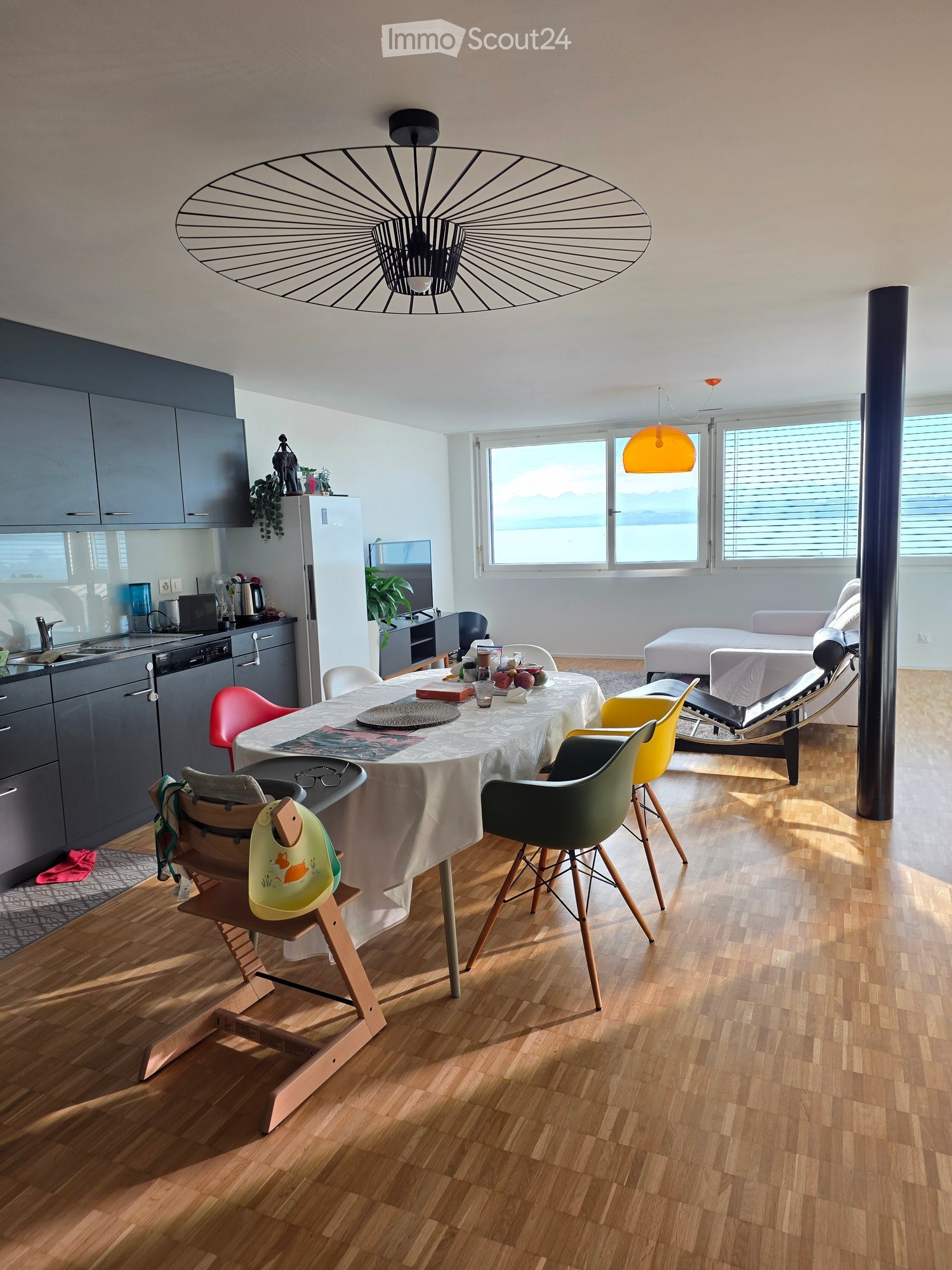 Open-plan living and dining area with modern furniture, including a dining table with chairs, a sofa, and a kitchen area with cabinets and appliances.