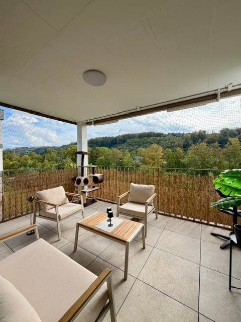Balcony with a scenic view of a forested area, featuring a tiled floor, a bamboo privacy screen, and a small seating area with chairs and a coffee table.
