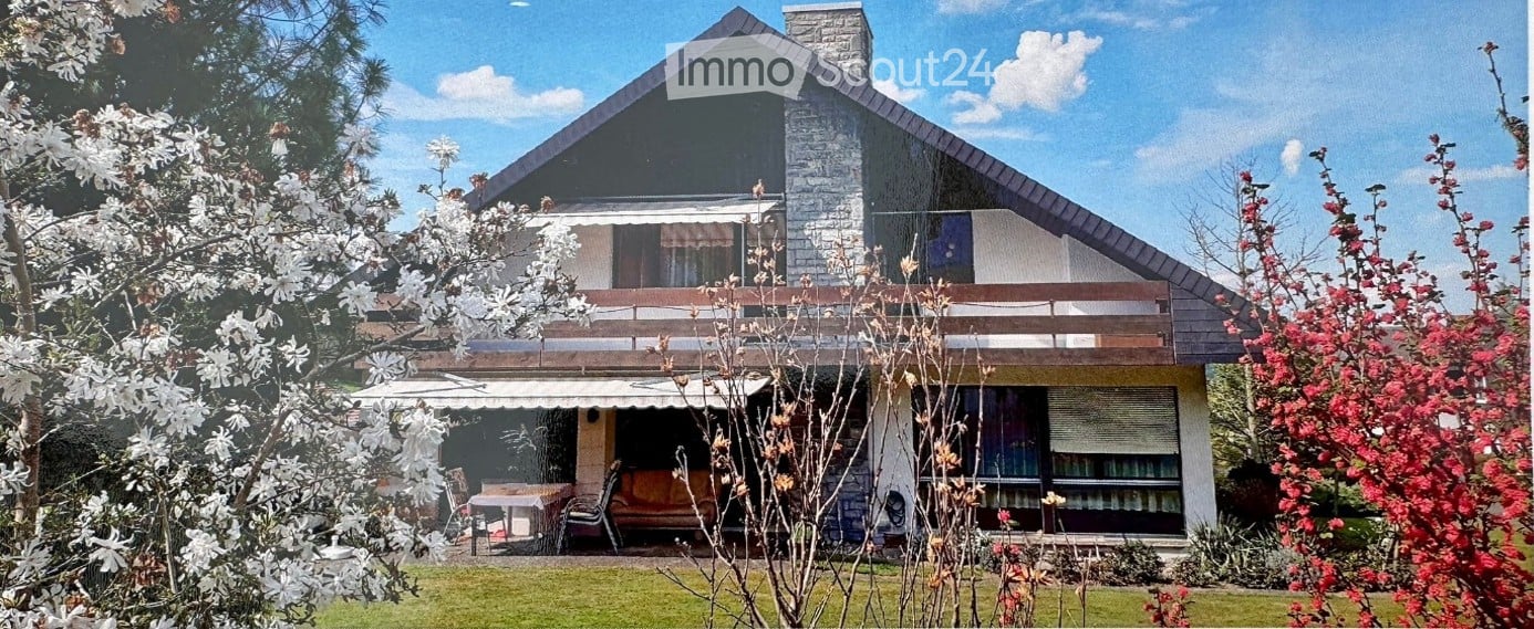 Two-story house with a stone chimney, large windows, and a balcony overlooking the garden.