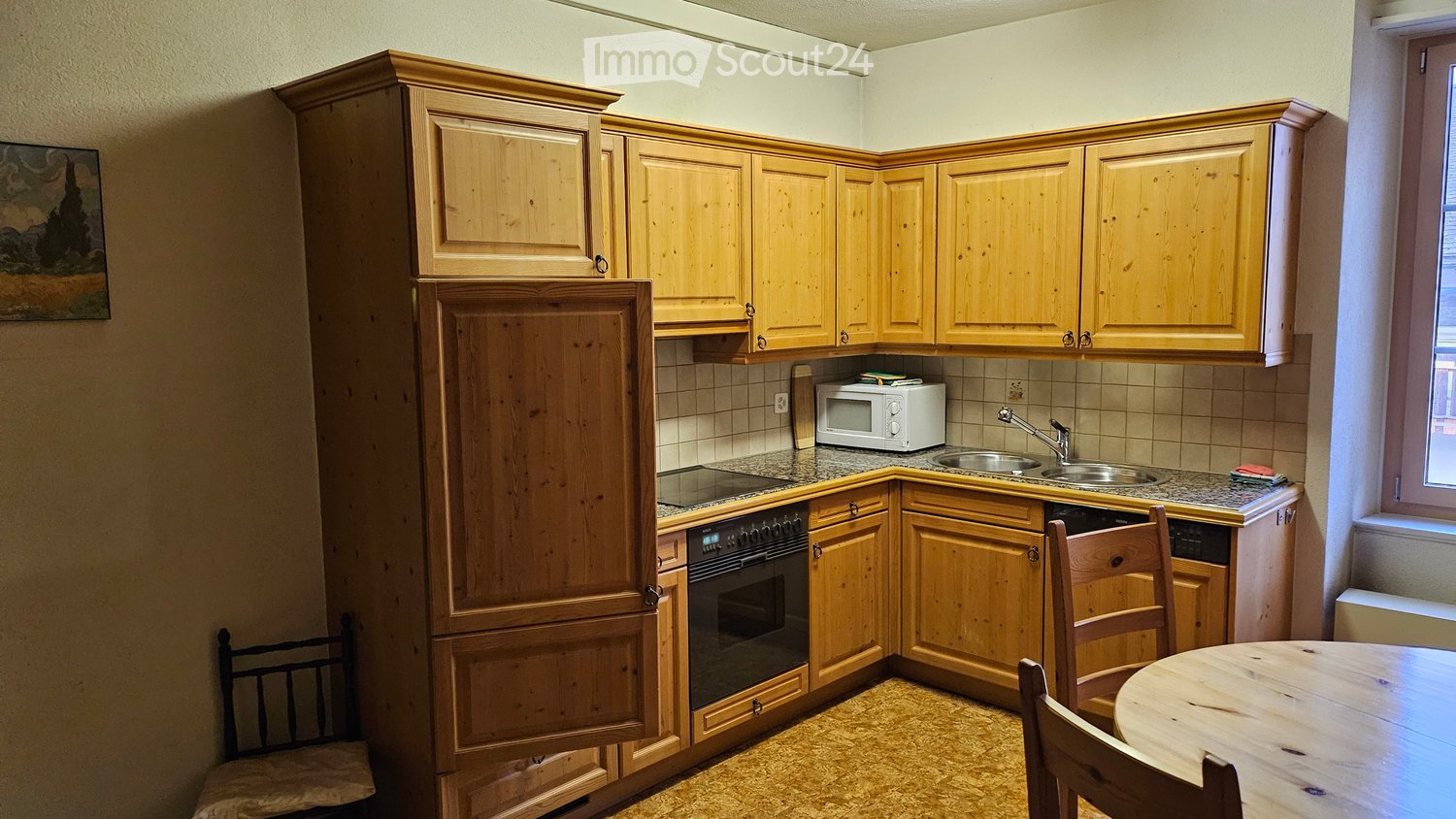 A cozy kitchen with wooden cabinets, a microwave, sink, oven, and a small dining area with a table and chairs.