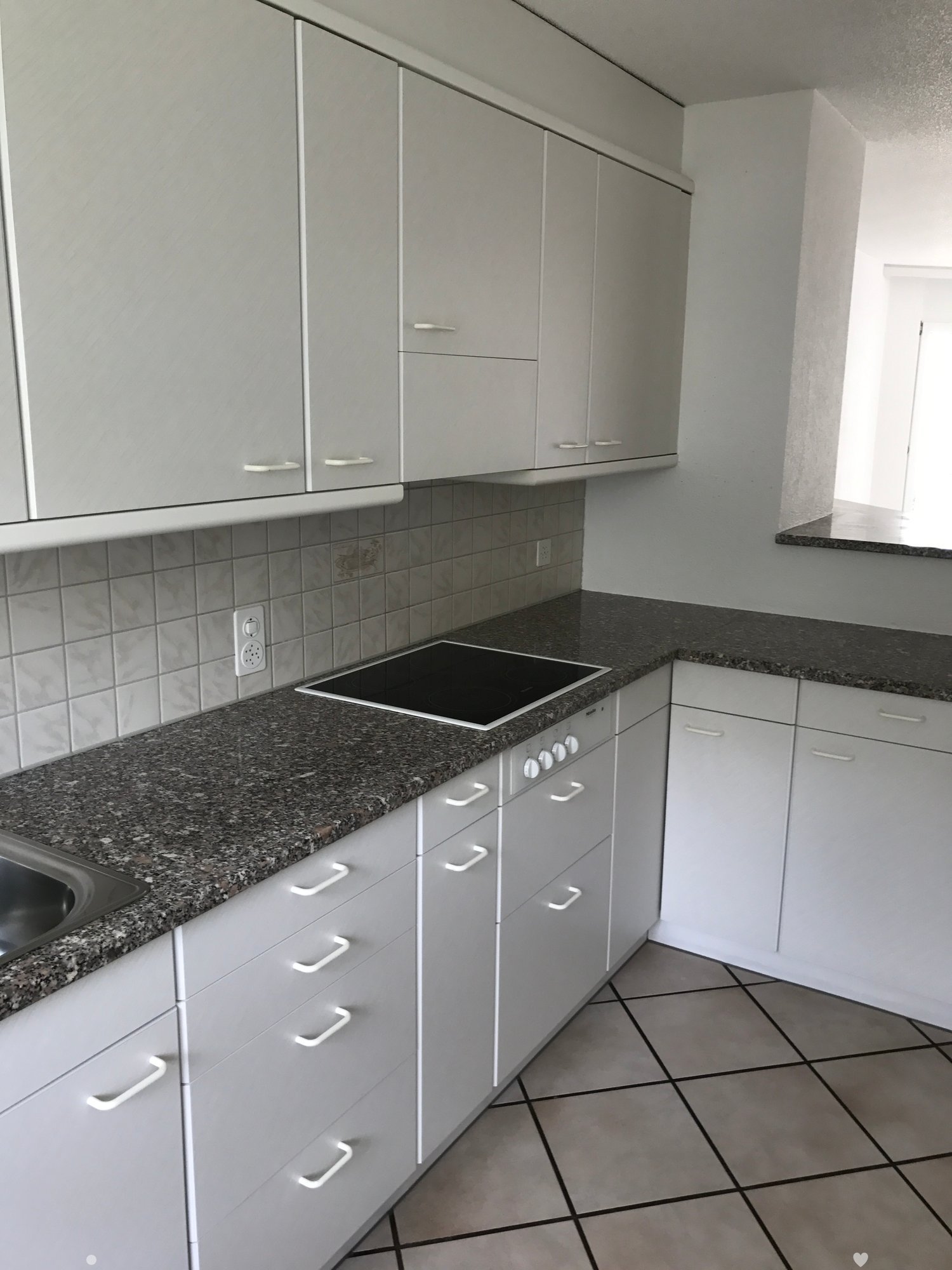 Modern kitchen with white cabinets, granite countertops, and an induction stove. The space features tiled walls and a tiled floor.