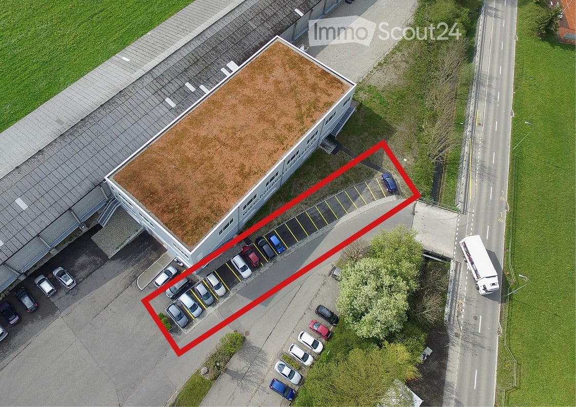 Aerial view of a commercial building with a flat roof and a parking lot with multiple cars.