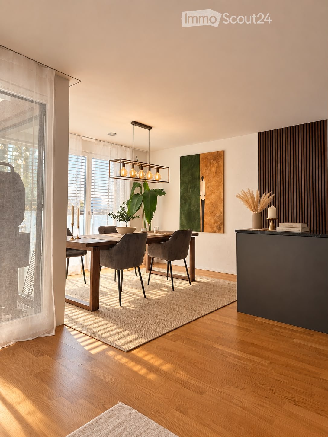 Modern dining area with a wooden dining table, four chairs, pendant light fixture, decorative bowl, candles, potted plants, artwork, and a countertop with books and a vase.