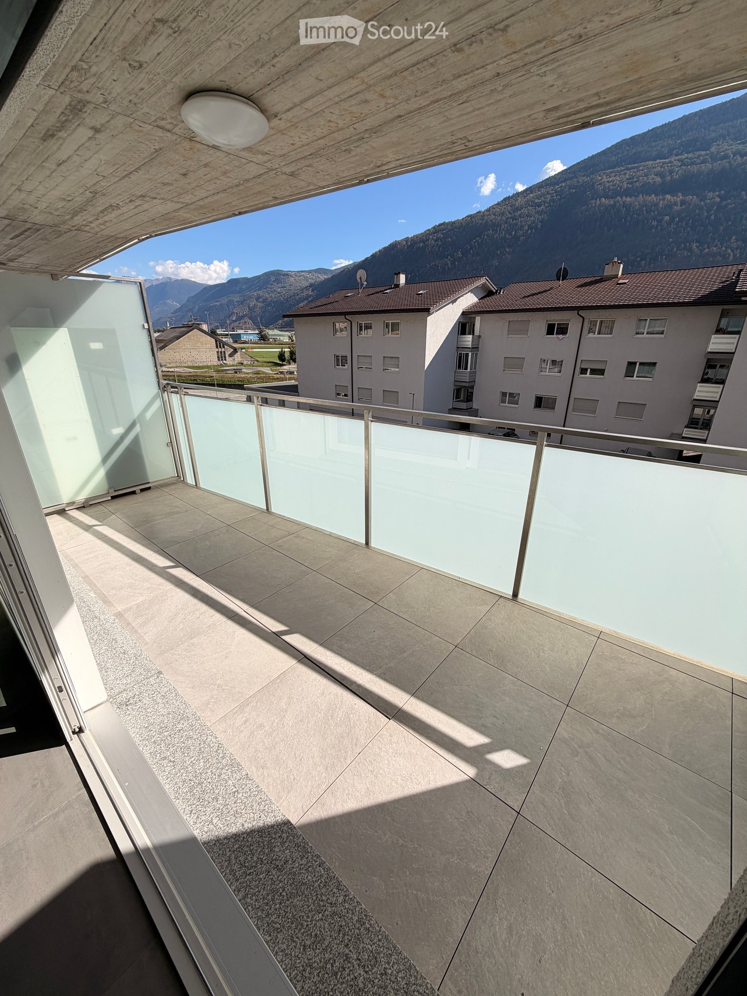Modern balcony with a glass railing, tiled floor, and a scenic mountain view in the background.