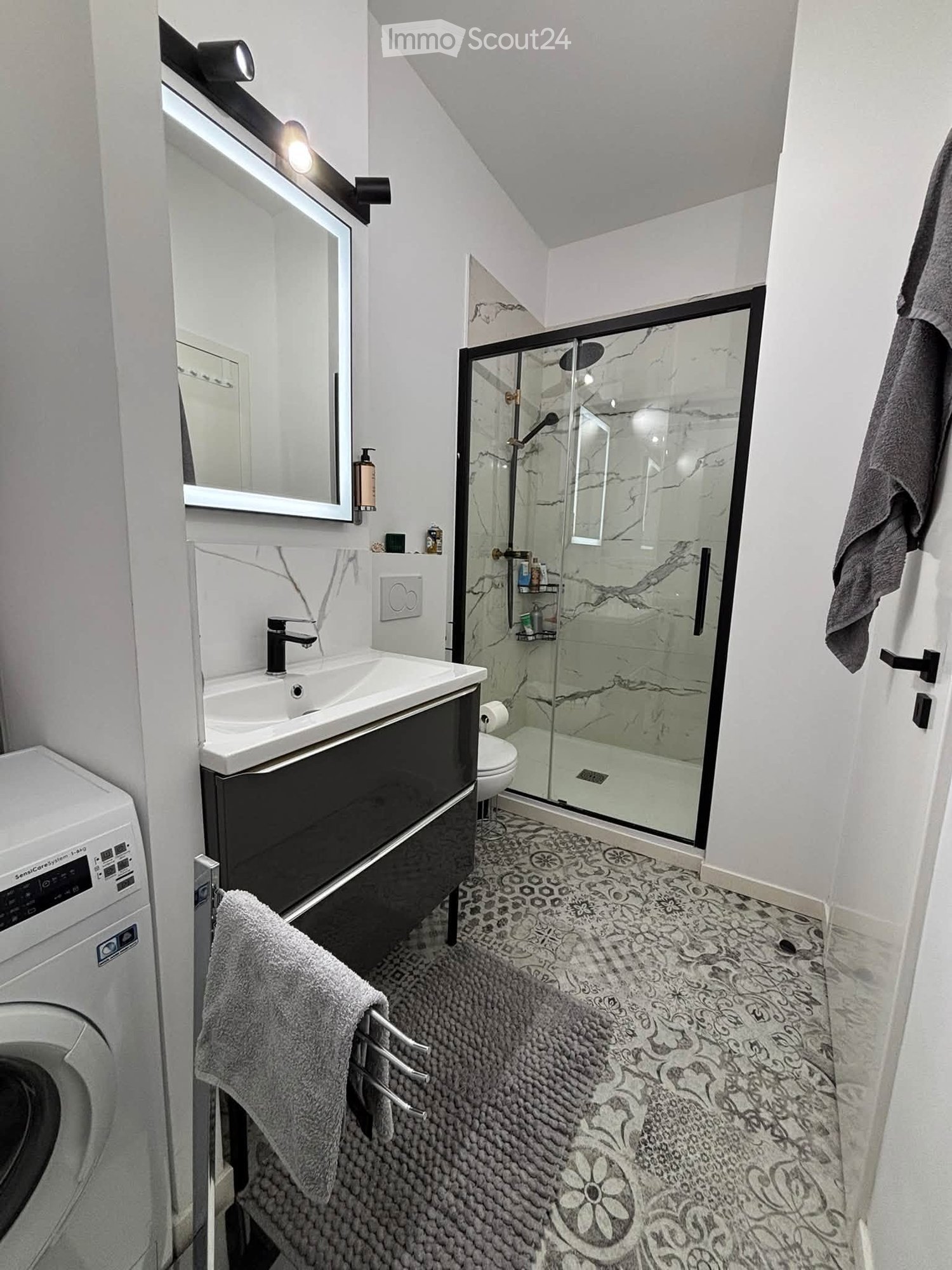 Modern bathroom with a white sink, black vanity, large mirror, glass-enclosed shower, and decorative tile floor.
