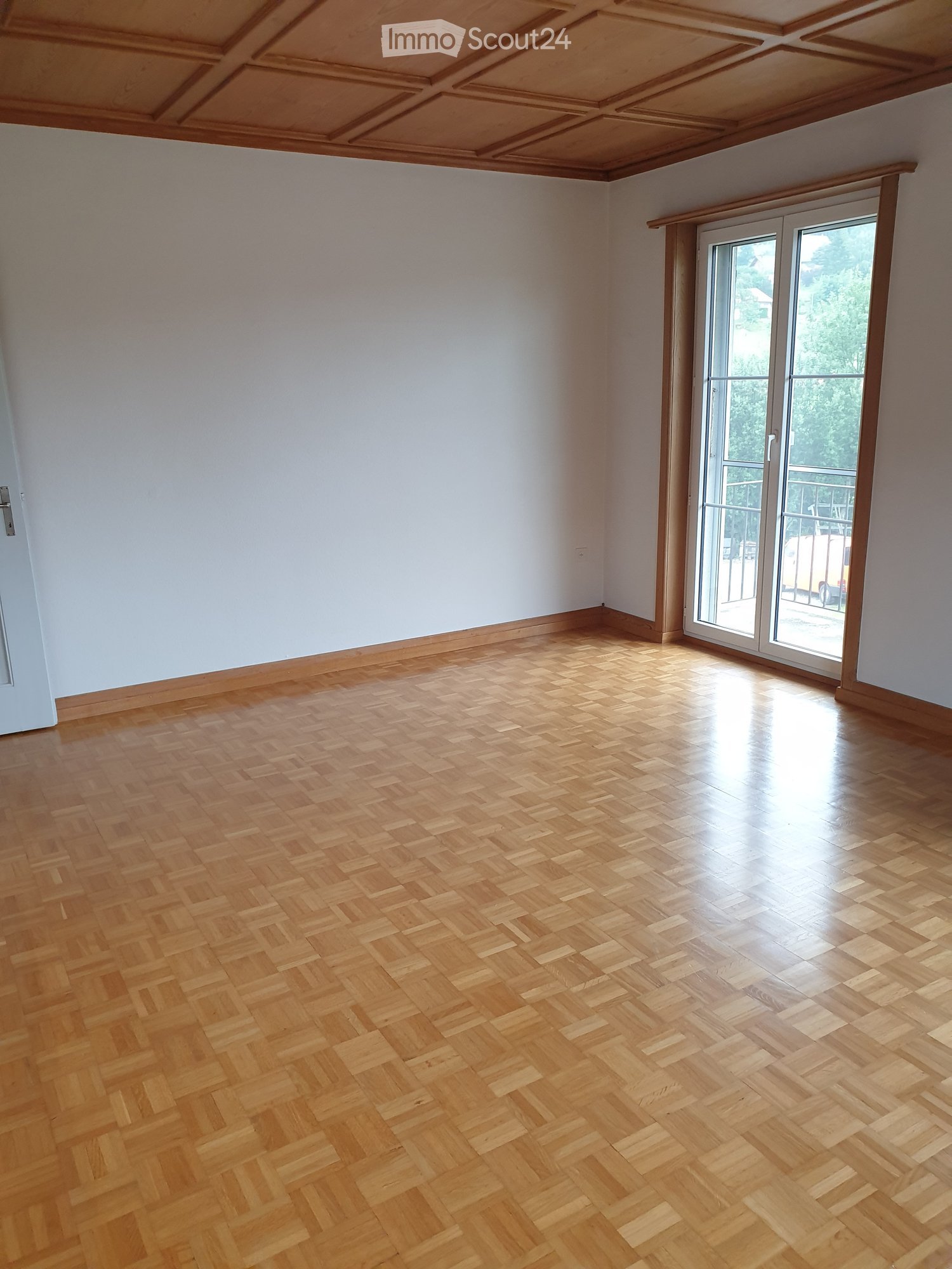Empty room with wooden herringbone flooring, white walls, and large sliding glass doors leading to a balcony.