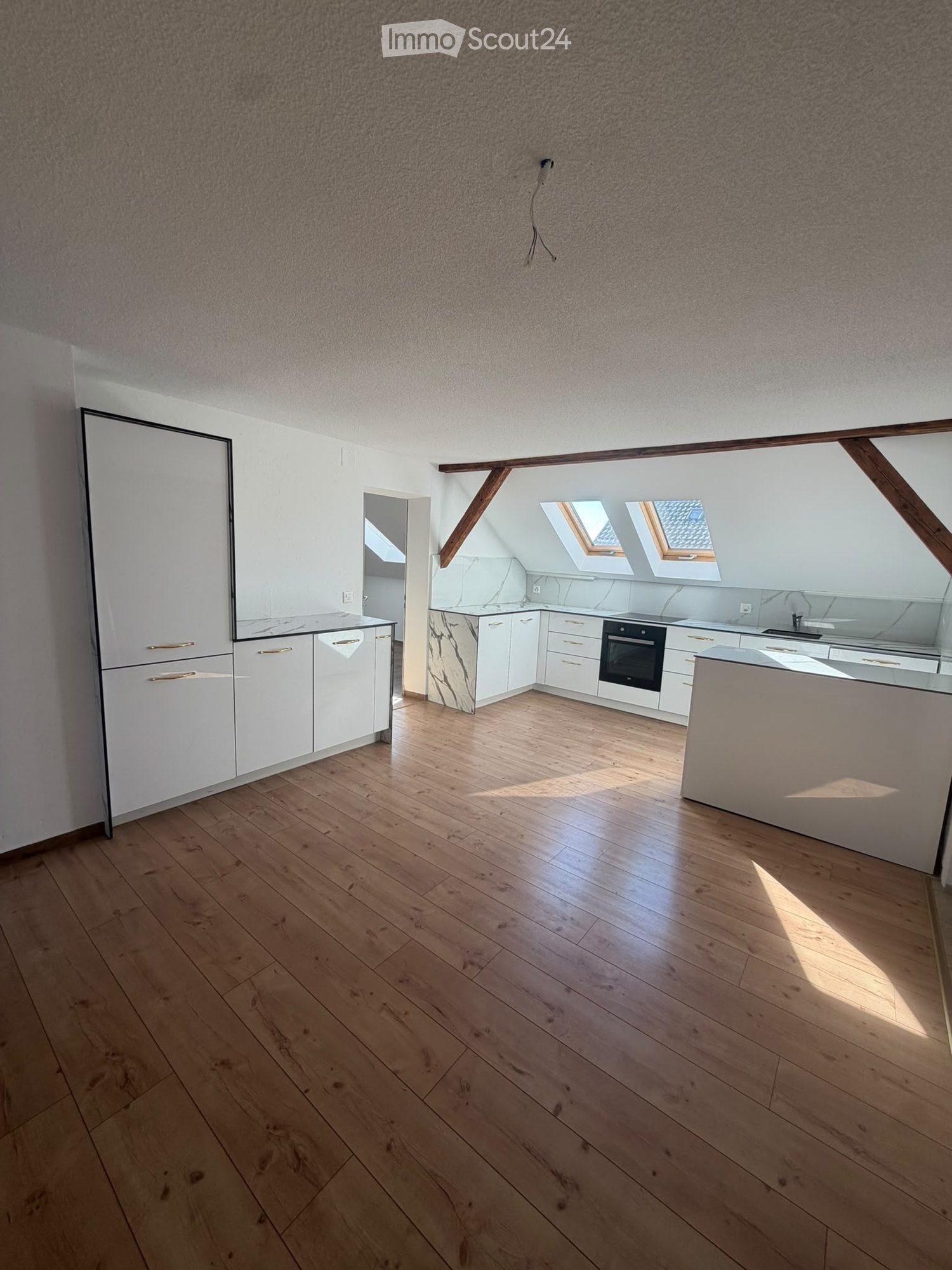 Empty room with wooden flooring, white cabinets, and skylight windows allowing natural light to enter.