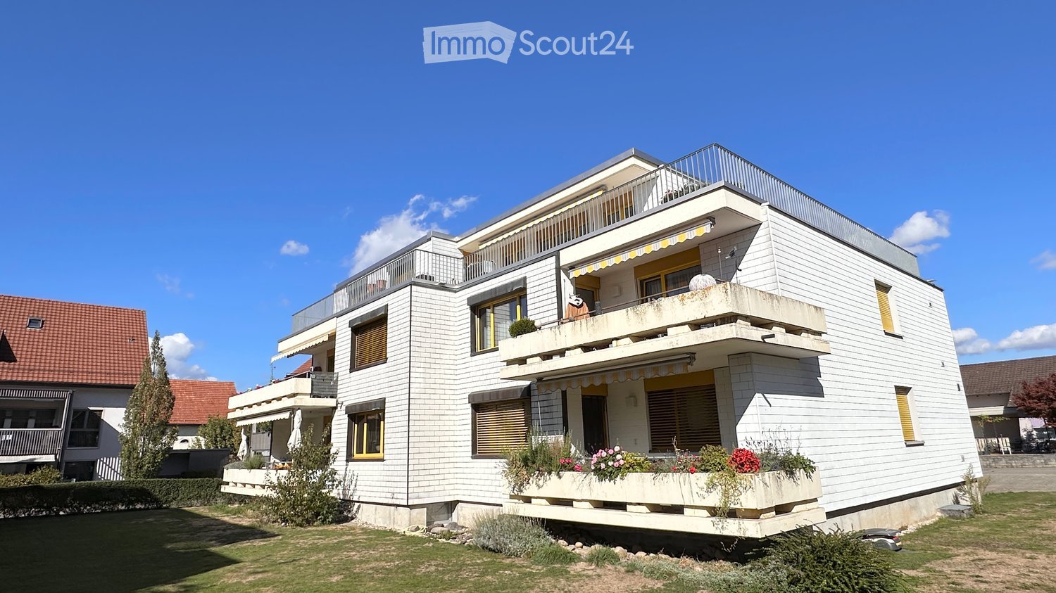 Modern two-story house with white siding, multiple balconies, and flower boxes. The house features large windows and a clean, contemporary design.