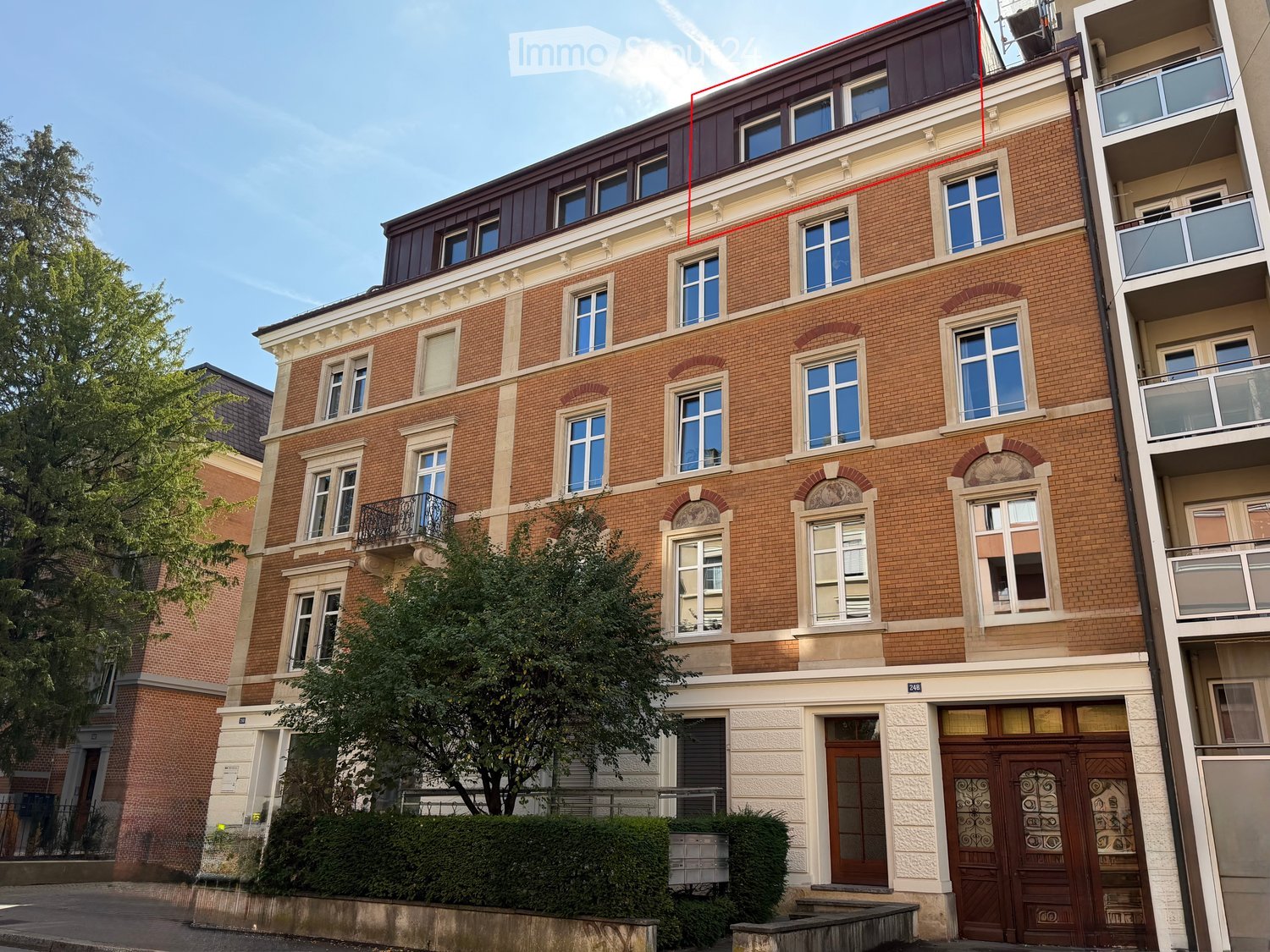 Four-story brick building with multiple windows, decorative balconies, and ornate wooden doors at the entrance.