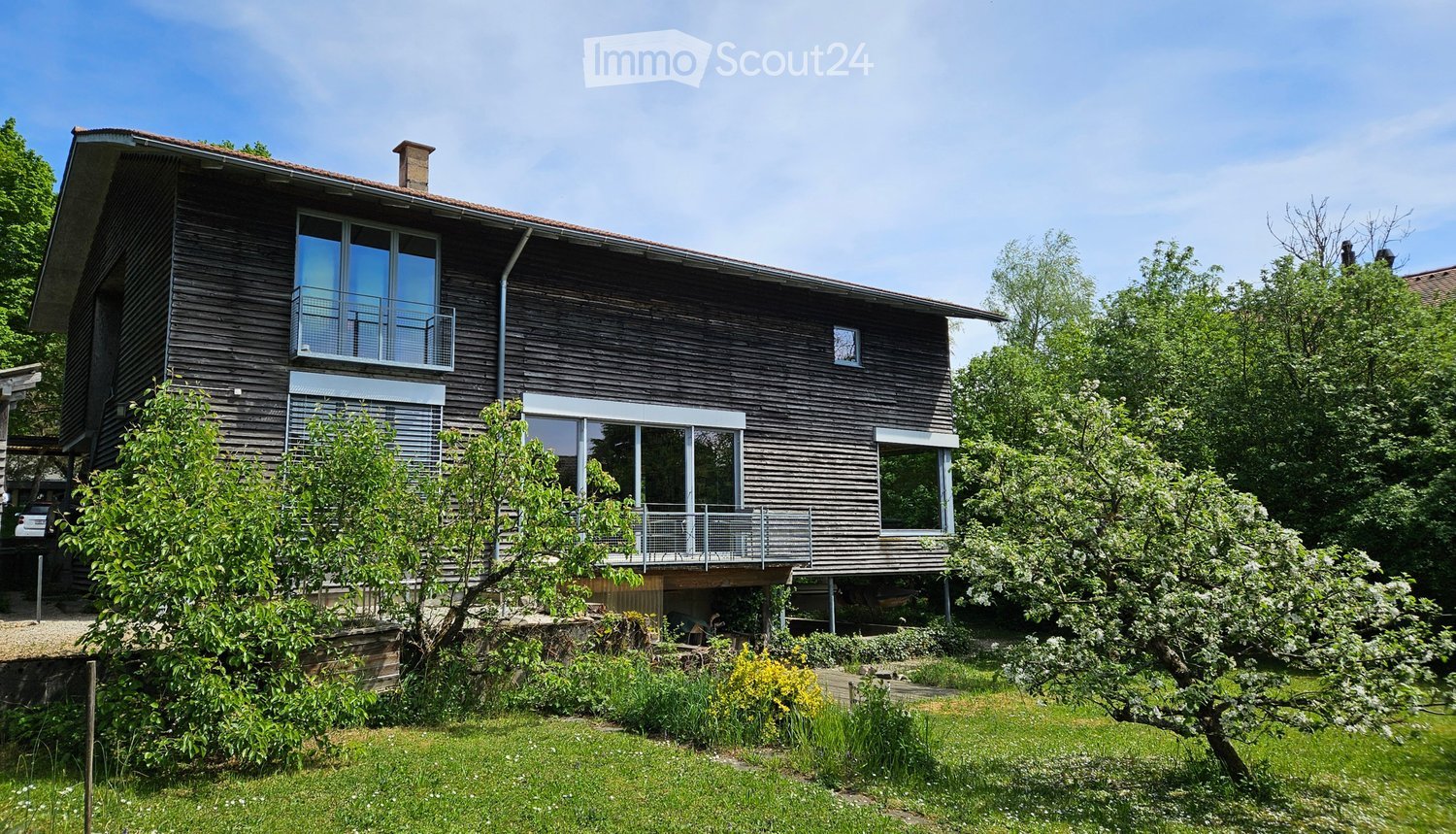 Two-story wooden house with large windows, balconies, and a well-maintained garden.