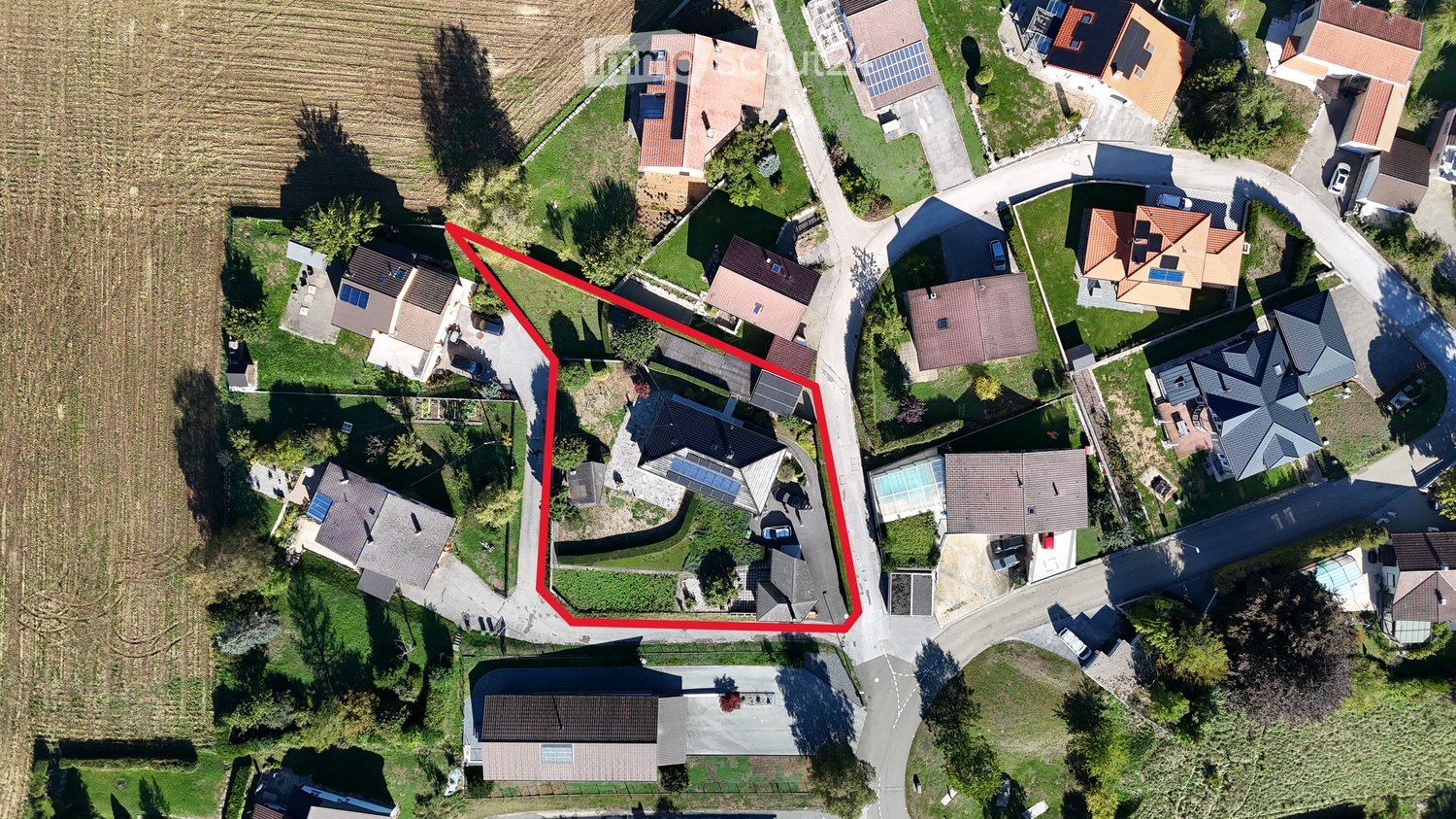 Aerial view of a residential area with multiple houses, gardens, driveways, and surrounding greenery.
