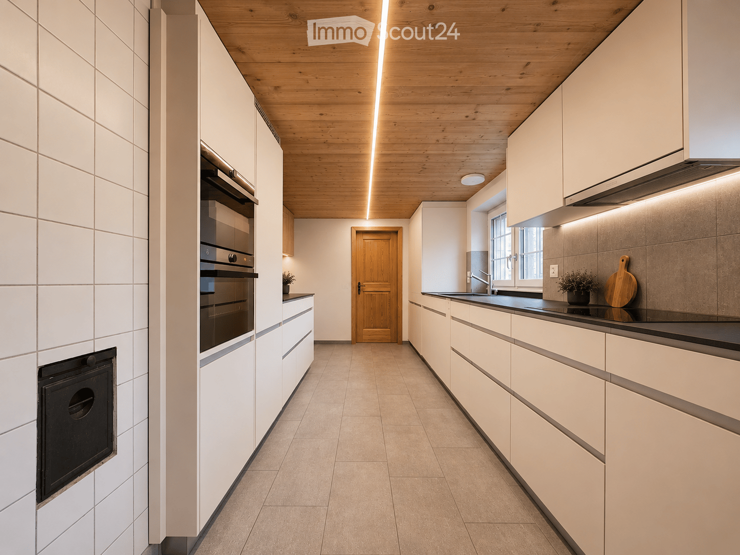 Modern kitchen with white cabinets, wooden ceiling, built-in oven, sink, and small potted plant on the counter.