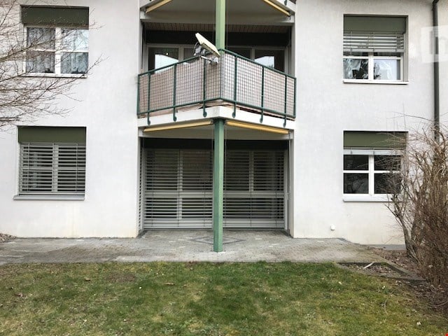 Modern multi-story building with a balcony, garage, and satellite dish on the roof.