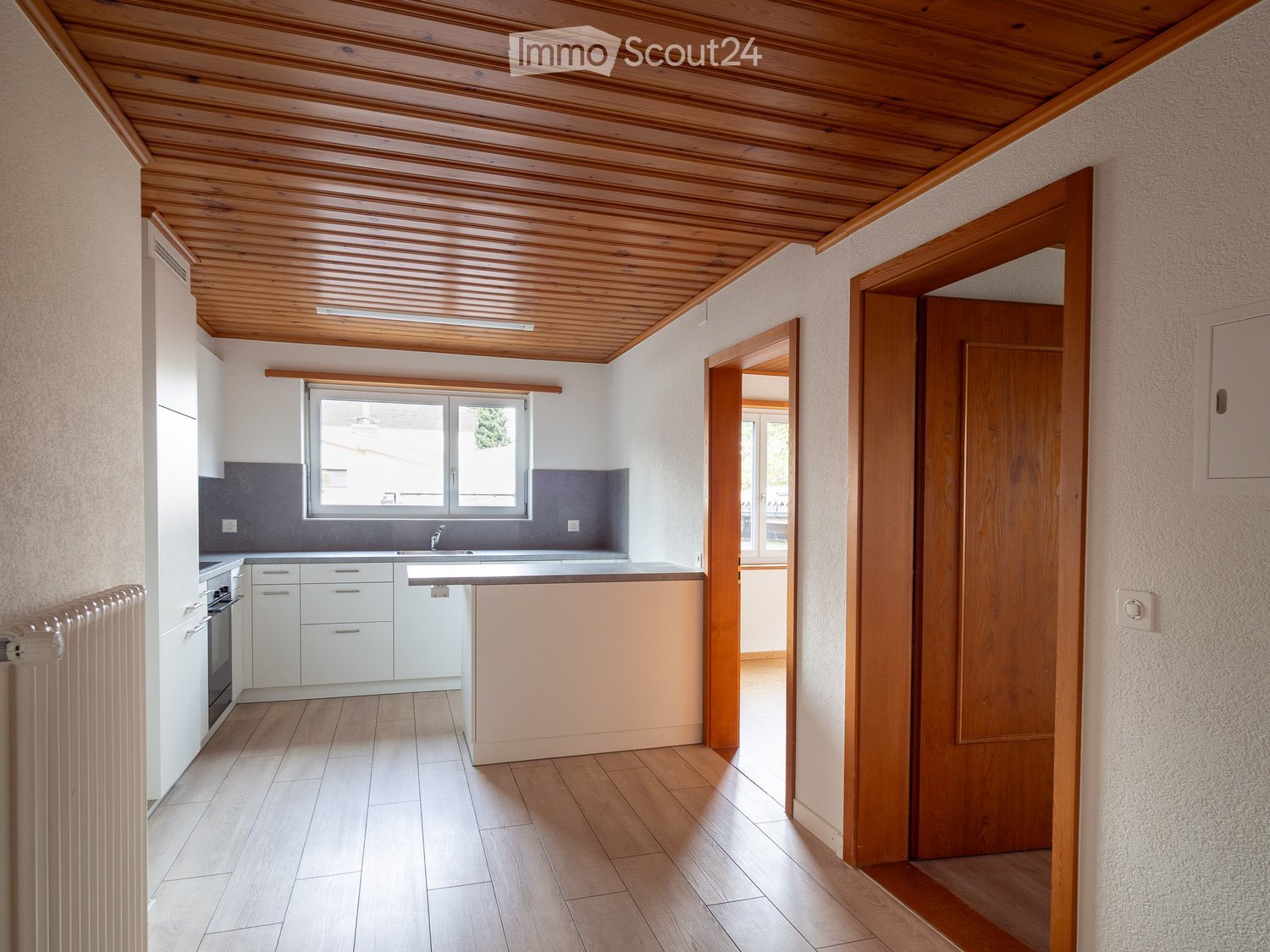 Modern kitchen with white cabinets, a central island, and a window above the sink. The space features wooden flooring and a wooden ceiling with exposed beams.
