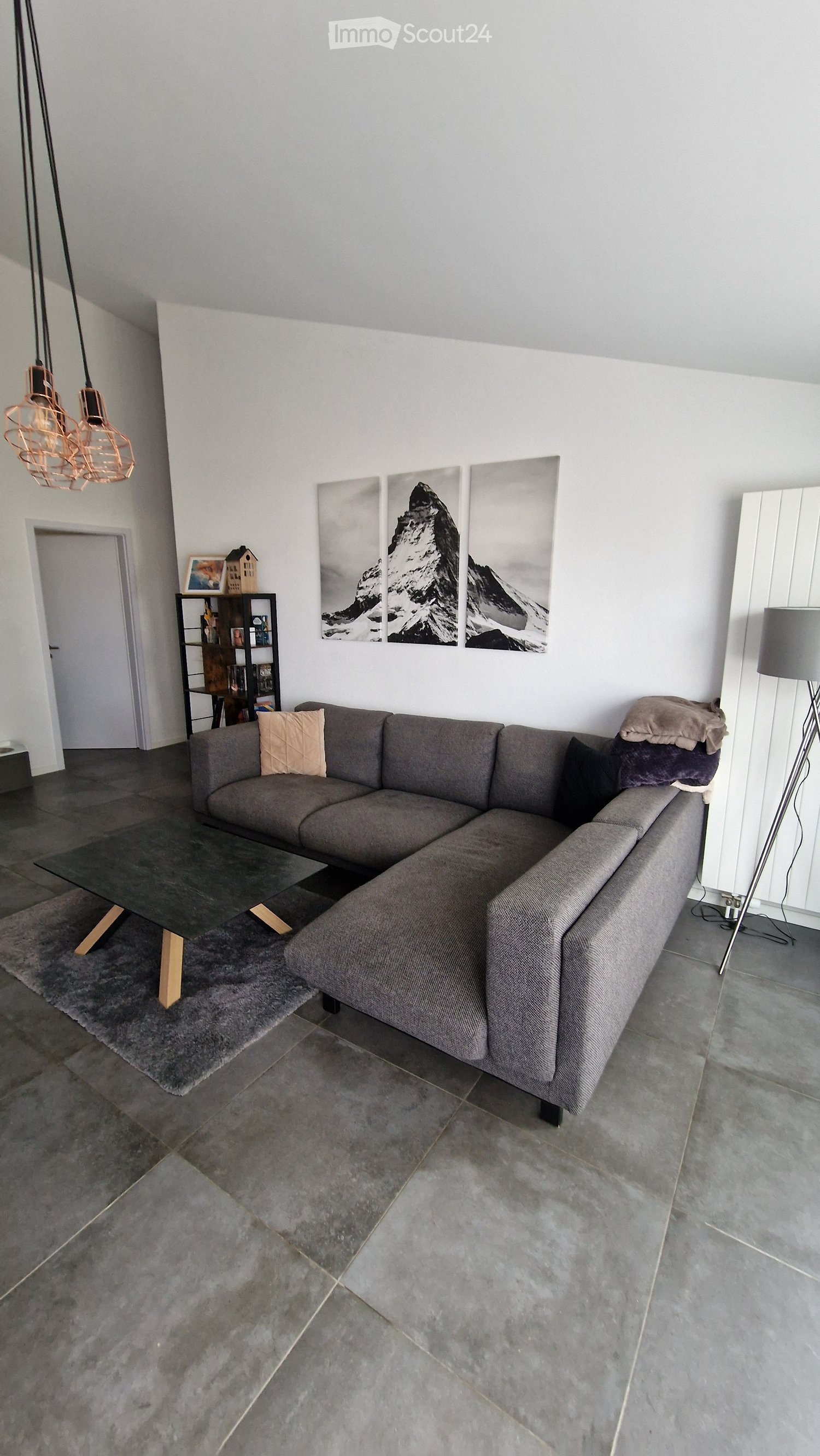 Modern living room with a grey sectional sofa, glass coffee table, floor lamp, and decorative wall art.
