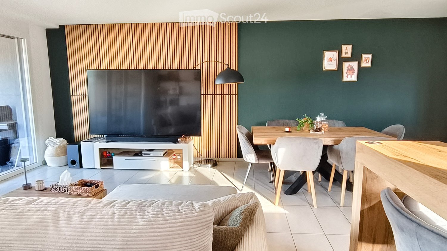 Modern living and dining area with a large television, sofa, dining table, chairs, and decorative items.