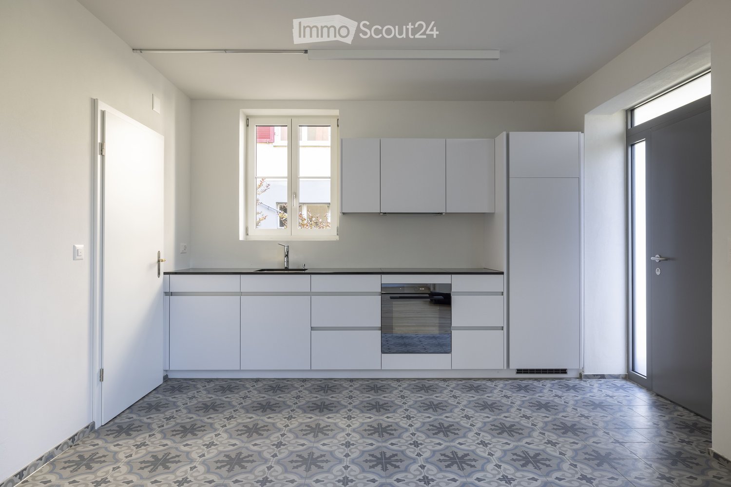 Modern kitchen with white cabinets, a sink, an oven, and a patterned tile floor.