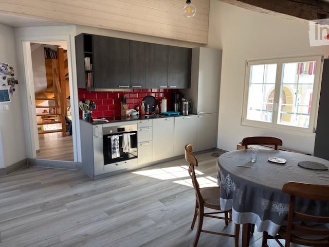 Modern kitchen with grey cabinets, red brick backsplash, white countertops, and stainless steel appliances. Includes a dining area with a round table and chairs.