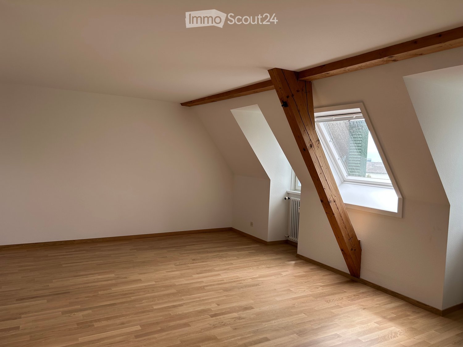 Empty attic room with wooden floors, slanted ceilings, and a skylight window.