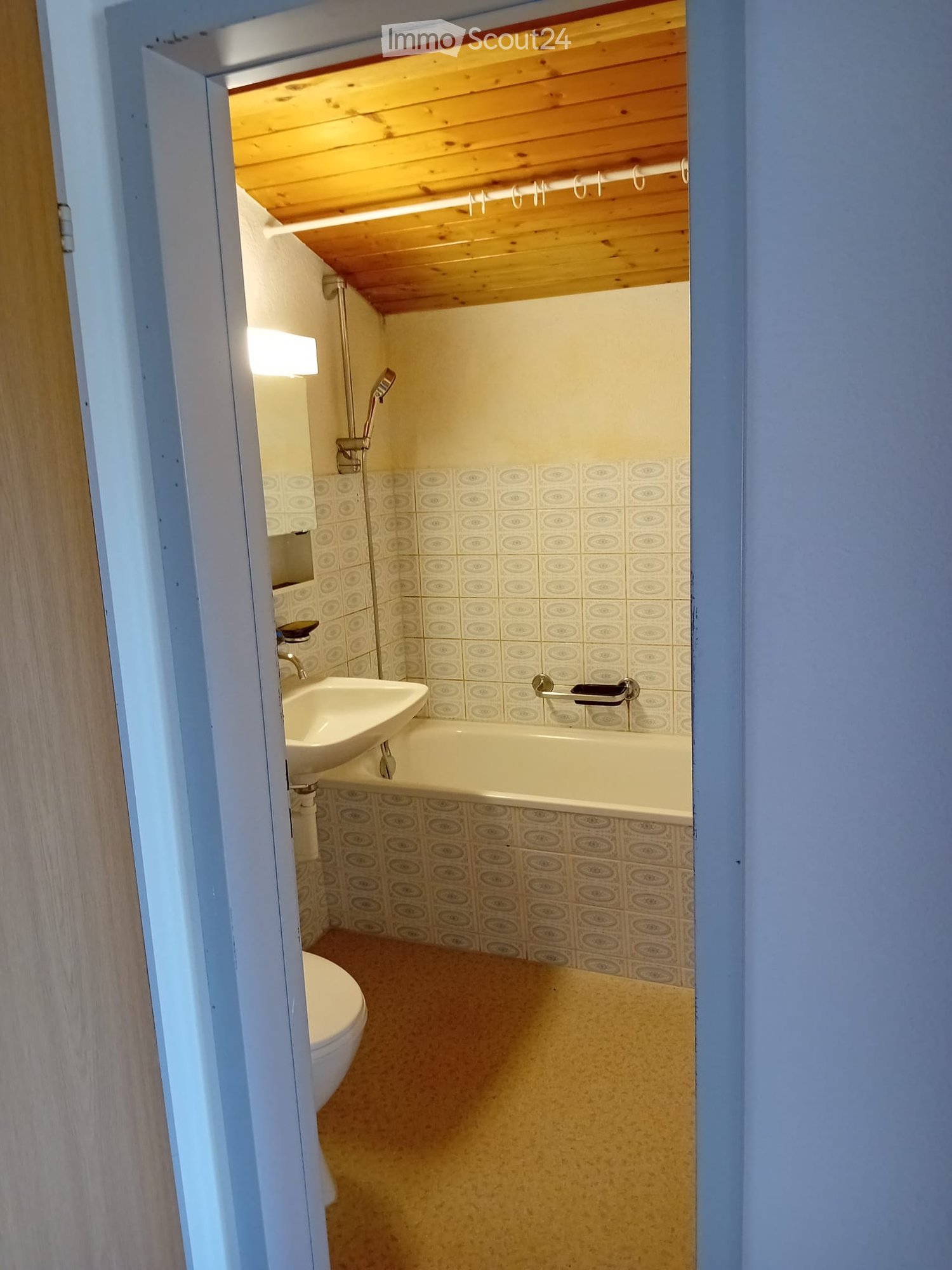 Compact bathroom with a sink, bathtub, toilet, and showerhead. Features patterned tiles and a wooden ceiling.