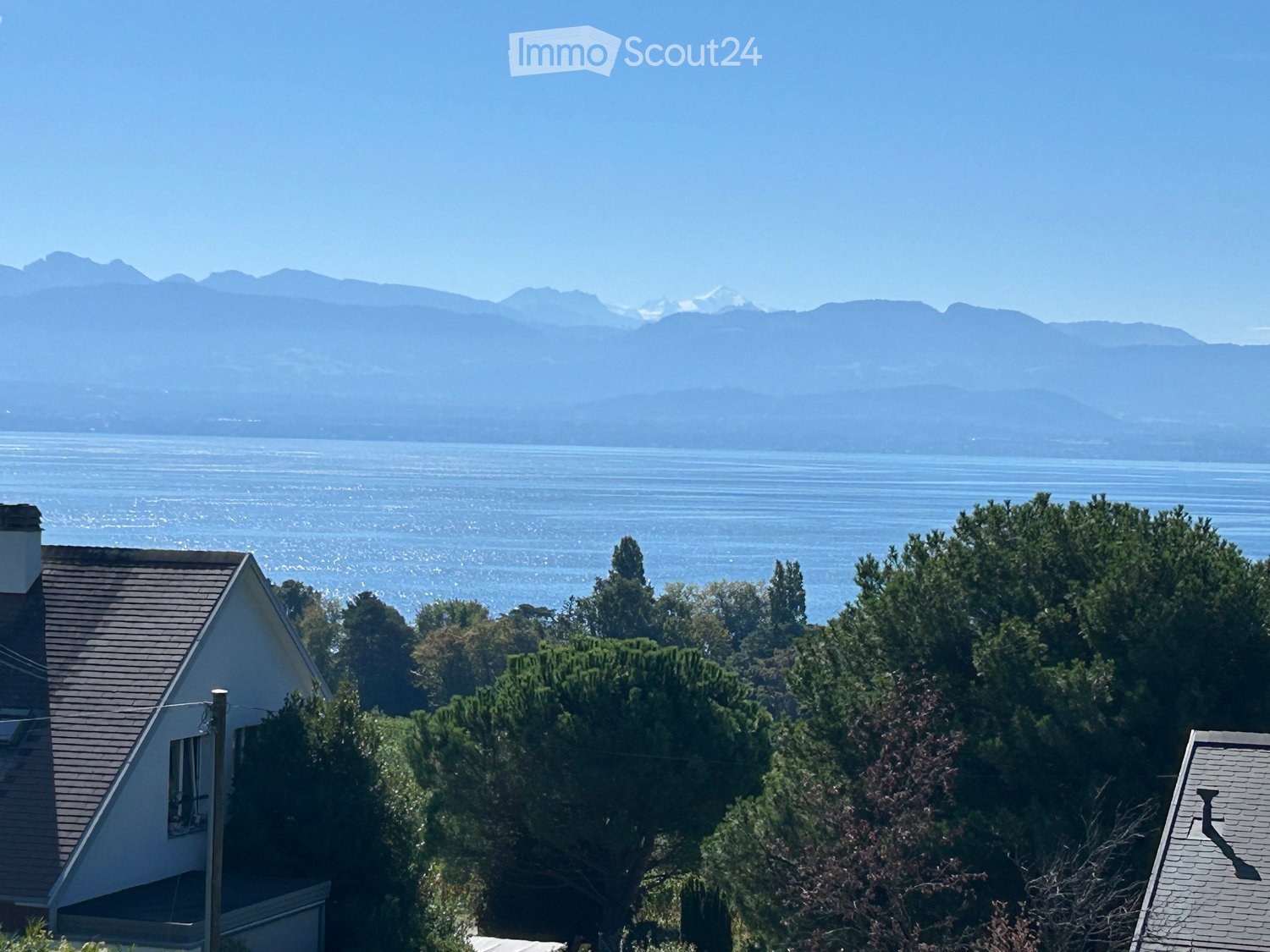 View of a house with a scenic backdrop of mountains and a body of water, surrounded by trees.