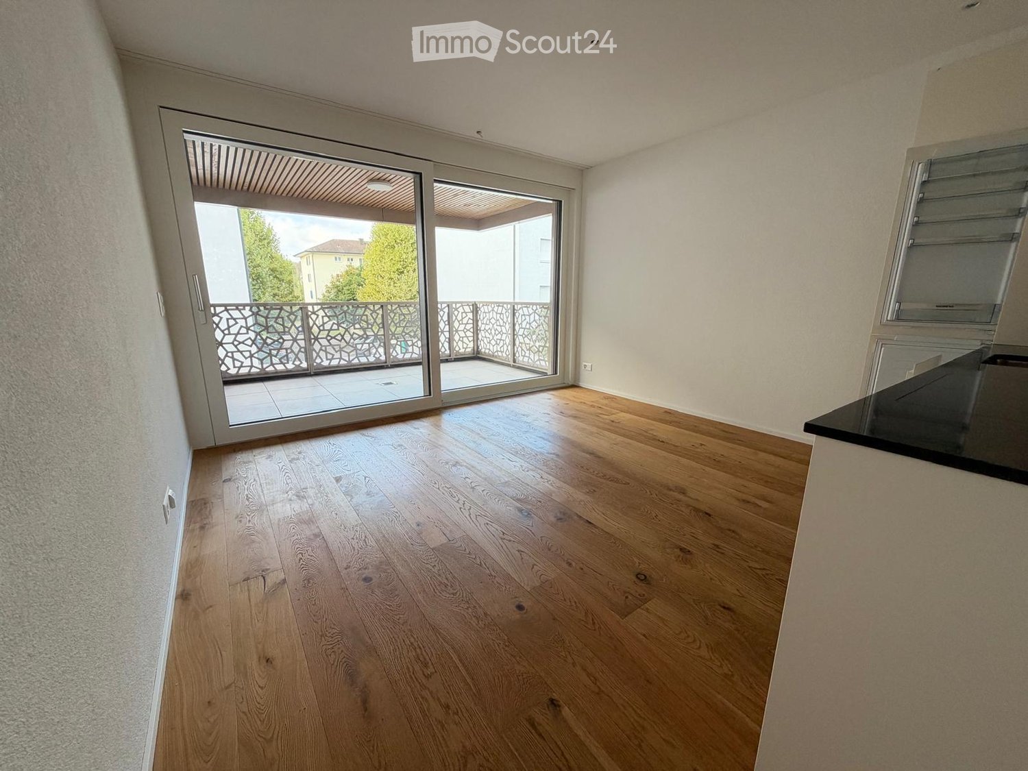 Empty room with light wooden flooring, white walls, and large sliding glass doors leading to a balcony.