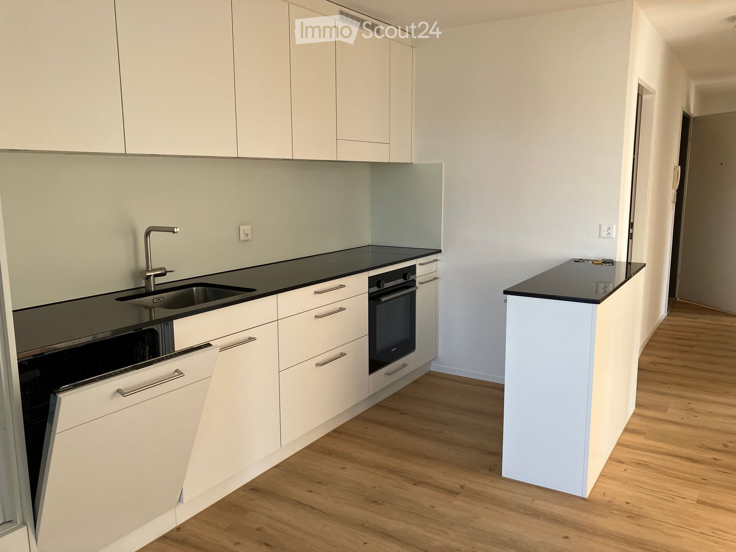 Modern kitchen with white cabinets, black countertops, a sink, and an oven. The floor is wooden.