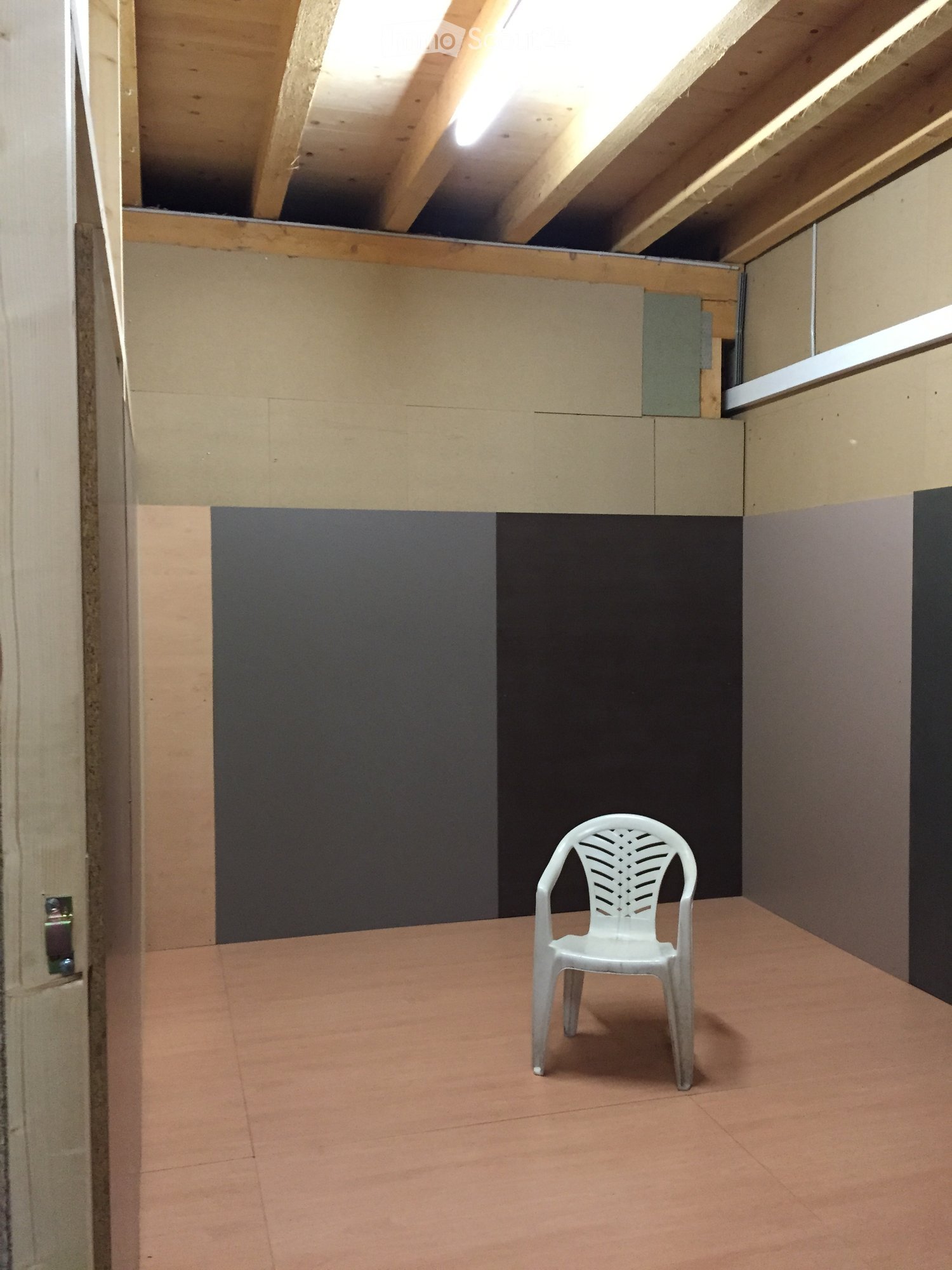 Empty room with beige tiled floor, exposed wooden beams on the ceiling, and a single white plastic chair in the center.