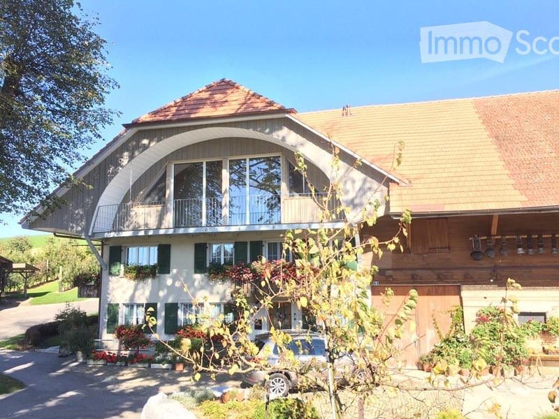 Two-story house with a large arched balcony, green shutters, and a well-maintained garden.