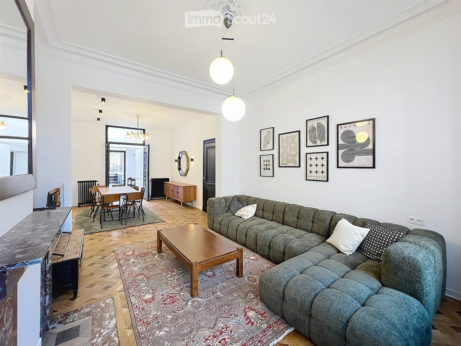 Spacious living room with a grey sectional sofa, wooden coffee table, dining area with a table and chairs, and decorative artwork on the walls.