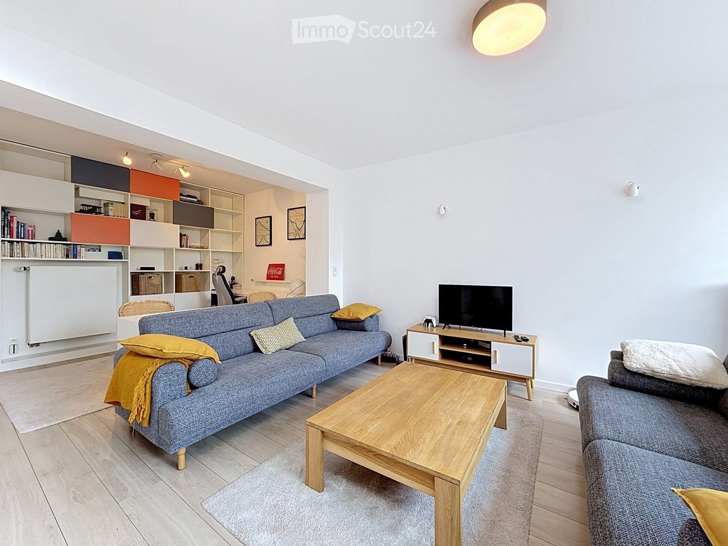 Modern living room with a grey sofa, wooden coffee table, TV stand, and shelves in the background.