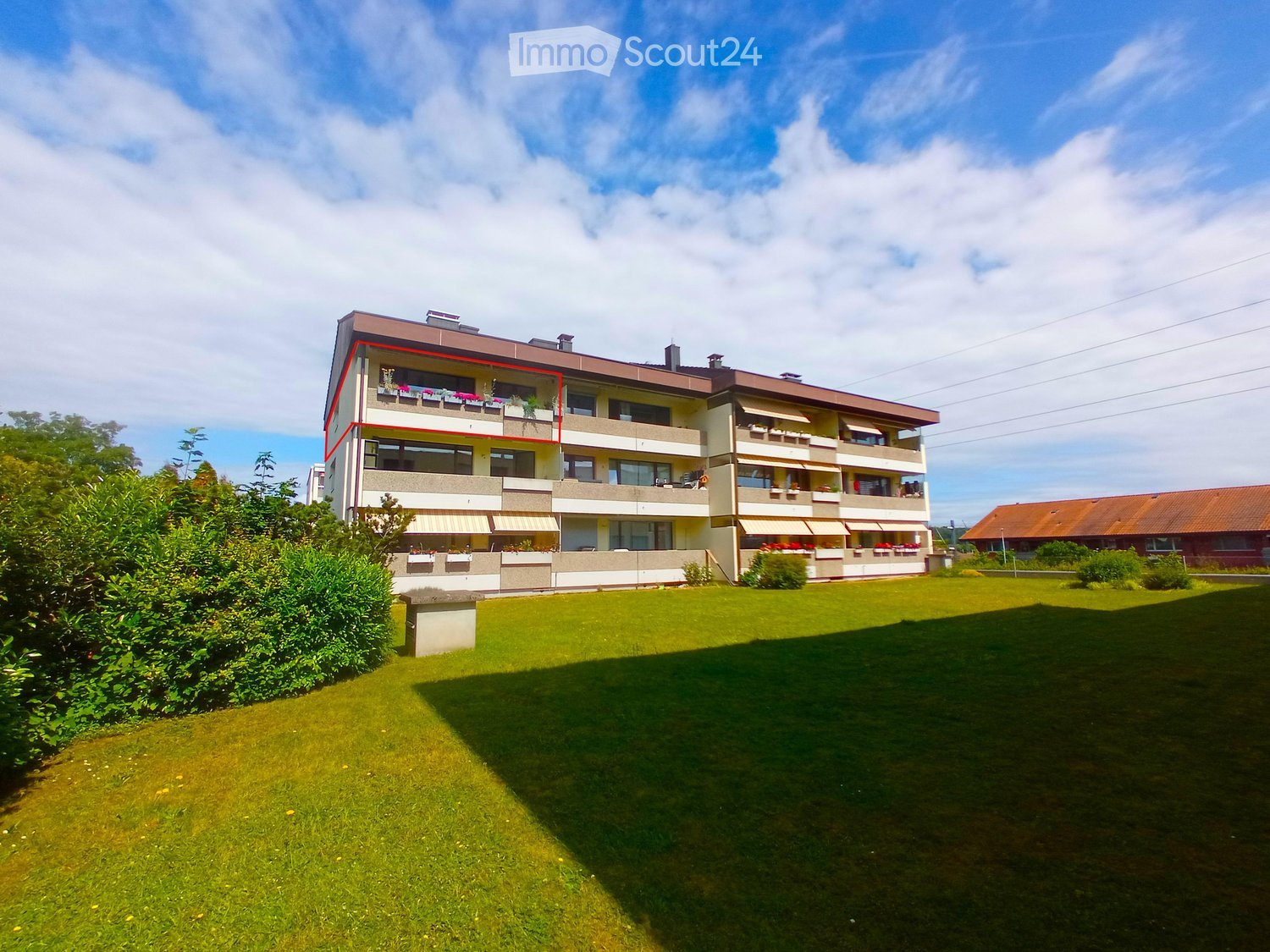 A multi-story residential building with balconies, surrounded by a well-maintained lawn and greenery.