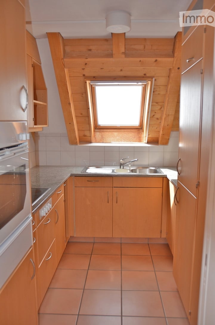 Bright kitchen with wooden cabinets, tiled floor, and a window above the sink.