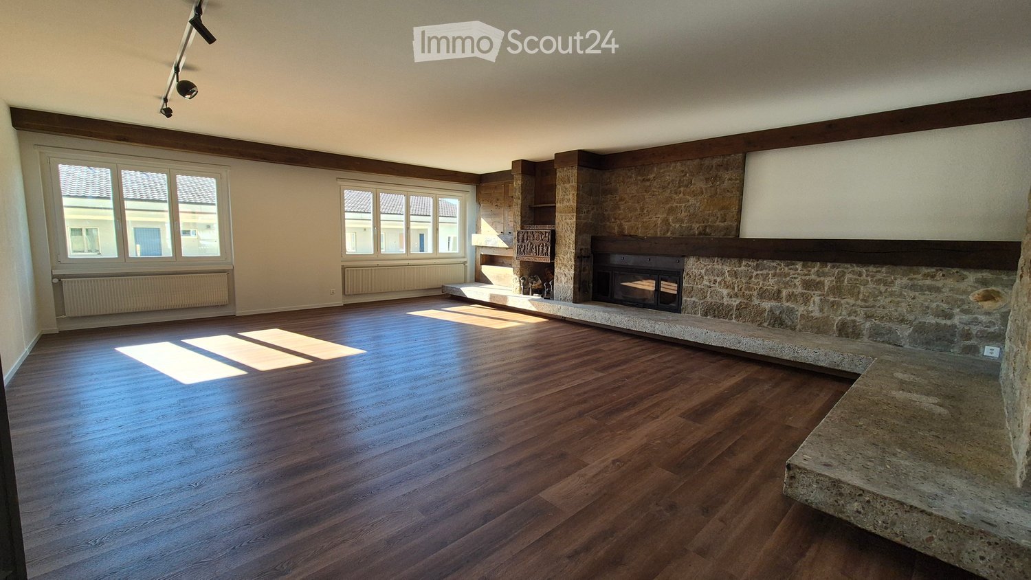 Empty room with wooden flooring, large windows, and a stone fireplace. No furniture or equipment present.